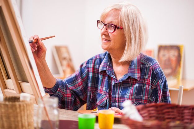 Elderly woman is painting in her home. Retirement hobby. woman painting as one of her hobbies