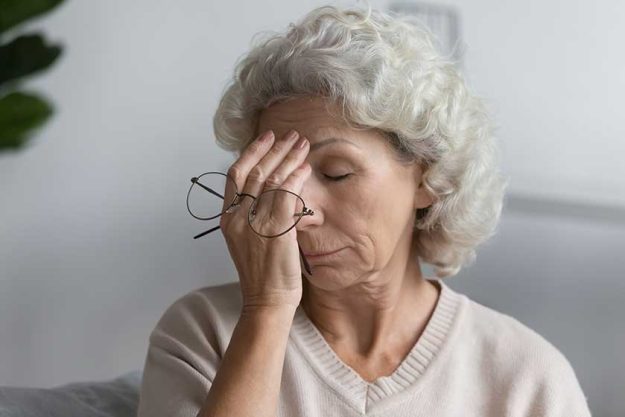 Tired senior lady holding glasses and rubbing face with closed eyes at home. Tired senior lady holding glasses and rubbing face with closed eyes at home.