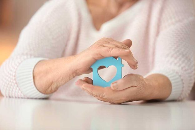 Senior woman with house figure at table. Home care concept Senior woman with house figure at table. Home care concept