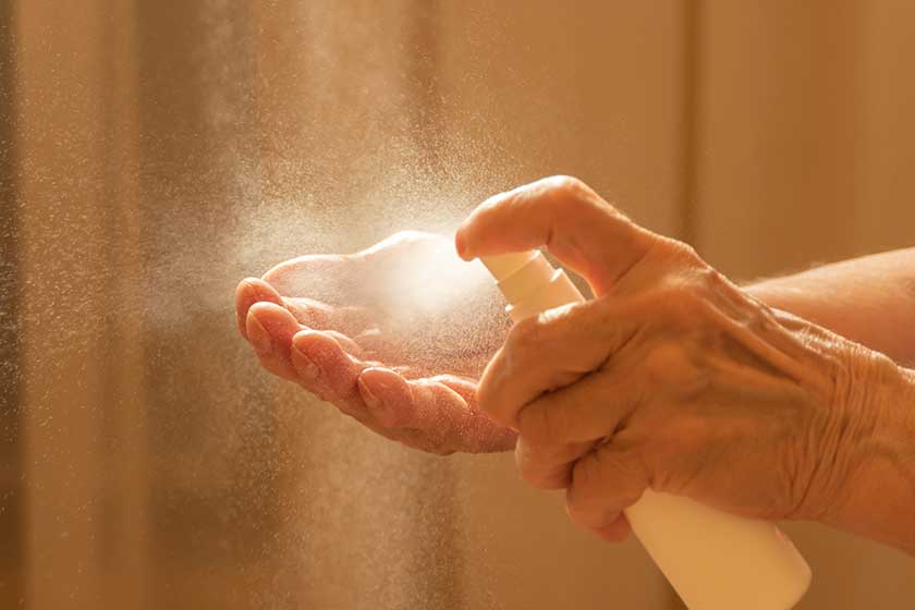 Older caucasian woman applying alcohol spray cleaning hands