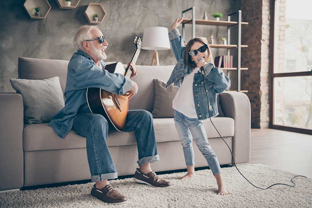 Photo of two people grandpa play guitar little granddaughter mic singing rejoicing cool style trendy sun specs denim clothes repetition school concert stay home quarantine living room indoors