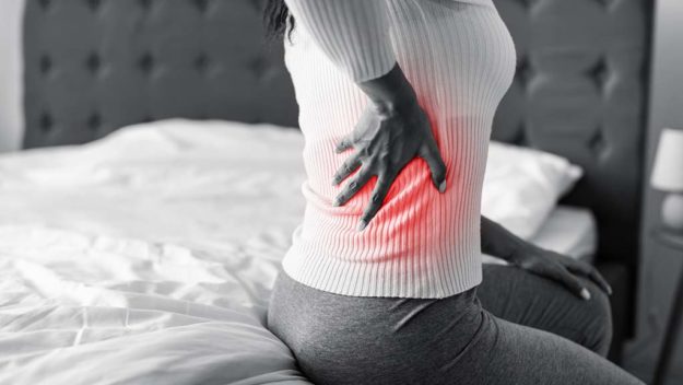 Woman with side back pain sitting on bed at home Ways To Relieve UTI Pain At Night