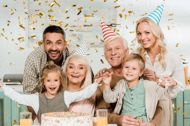 happy family sitting under falling confetti near birthday cake a happy family sitting under falling confetti near birthday cake and smiling at camera