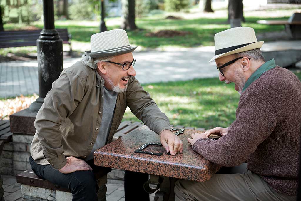 I won this game. Side view of happy old man putting last domino chip on table and smiling. His friend is looking at it with shock and shouting