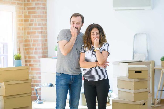 Middle age senior couple moving to a new home with boxes around looking stressed and nervous with hands on mouth biting nails. Anxiety problem. Middle age senior couple moving to a new home
