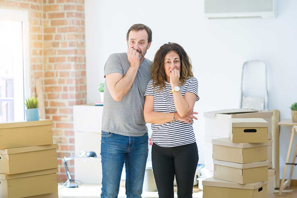 Middle age senior couple moving to a new home with boxes around looking stressed and nervous with hands on mouth biting nails. Anxiety problem. Middle age senior couple moving to a new home