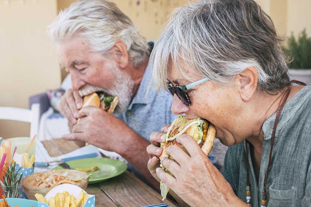 People eating hamburger junk food - Couple of senior man and woman with fast food lunch time