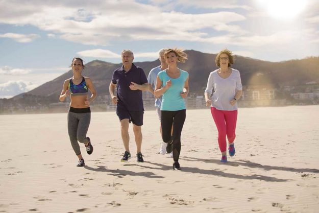 Senior people and sports coach running on sandy beach