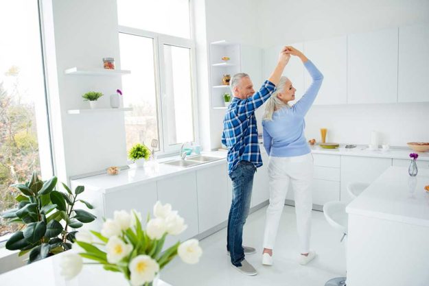 Side view full size portrait of lovely stylish attractive creative couple in casual outfit dancing in pair in the kitchen, enjoying morning, spending time together, woman making turn around