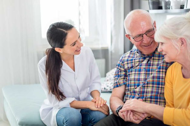 Smiling nurse talking with senior couple during home visit Smiling nurse talking with senior couple during home visit