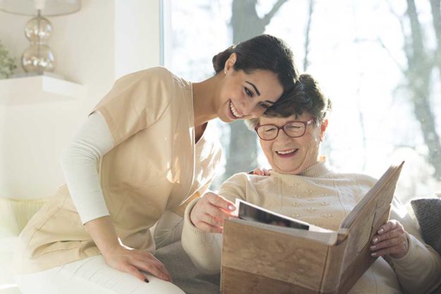 Smiling senior woman watching photobook with happy caregiver