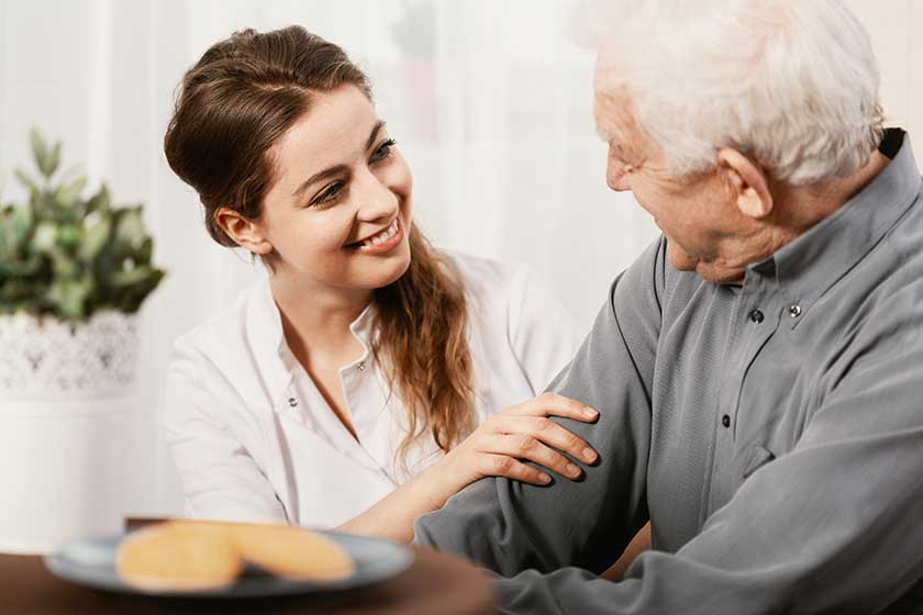 Smiling young nurse sitting at table with senior patient