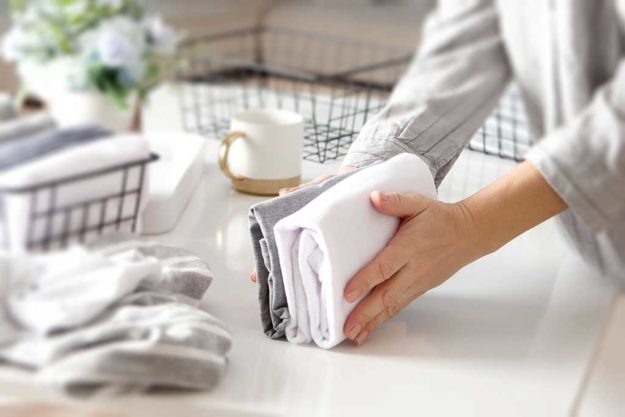 A woman folds her clothes and puts them in metal black baskets and boxes. Nordic style minimalism.