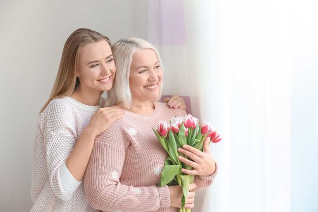 Young daughter and mother with bouquet of flowers at home