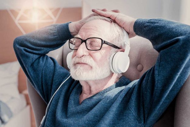 Nice relaxed aged man wearing headphones and closing his eyed while listening to music