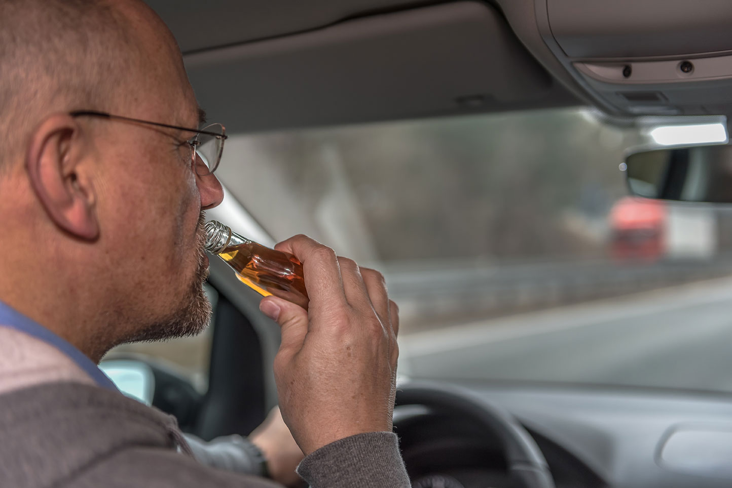 An elderly man drives a car and drinks alcohol while driving