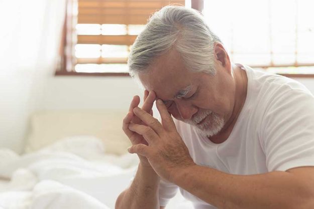 Asian Elderly man with a headache sitting on a bed in morning Asian Elderly man with a headache sitting on a bed in morning