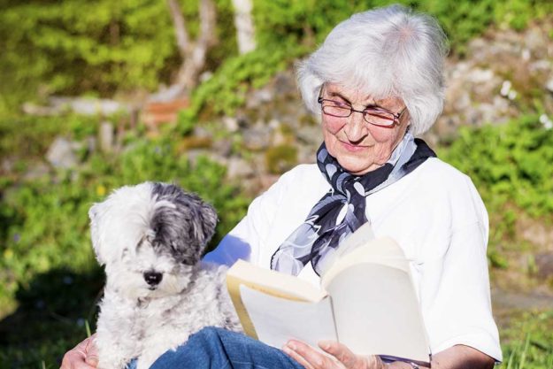beautiful senior woman reading book with her dog outdoor