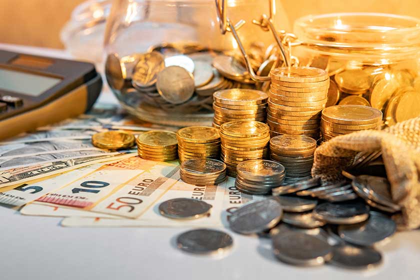 Calculator with coins stack and spilling out of money bag, dollar and euro banknotes on the table.