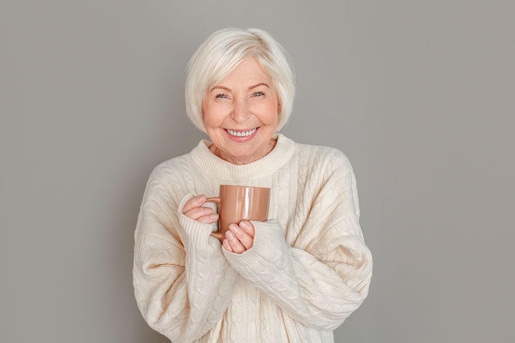 Senior woman in sweater studio isolated on grey wall drinking hot chocolate Senior woman in sweater studio isolated on grey wall drinking hot chocolate