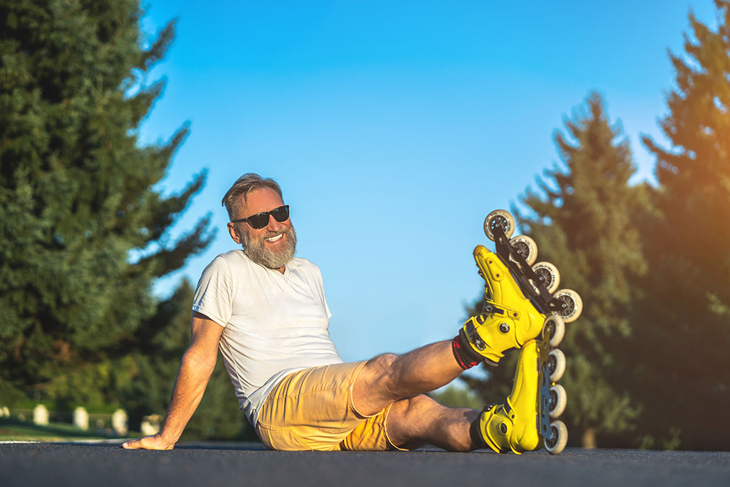 The happy old man with a roller skates sitting on the asphalt The happy old man with a roller skates sitting on the asphalt