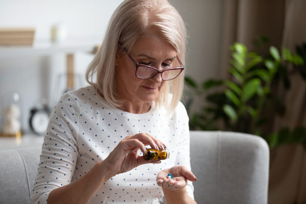 Elderly female pensioner having daily medicines at home Serious senior woman in glasses sit on couch having daily vitamins or diet supplements at home, mature old female pensioner take dose of pills from meds bottle, elderly healthcare, medication concept