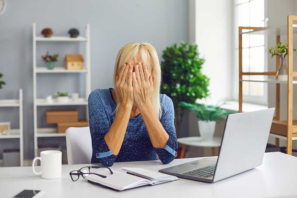 Frustrated senior woman covering face unable to deal with problem.