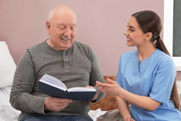 Nurse reading book with senior man in hospital ward. Medical assisting Nurse reading book with senior man in hospital ward. Medical assisting