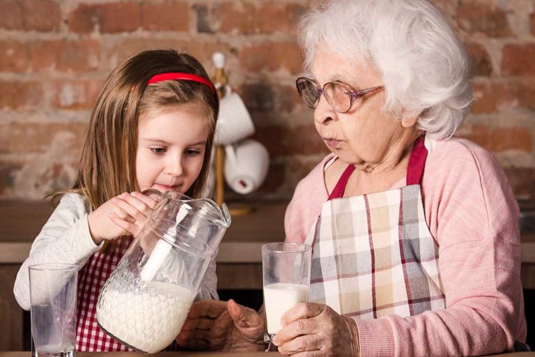 Senior grandmother with granddaughter drinking milk at kitchen