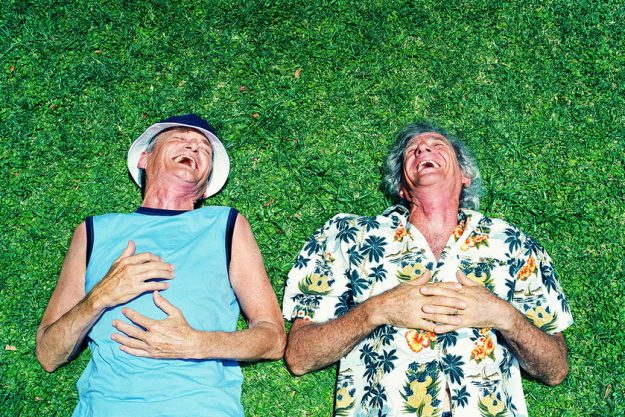 Two mature men lying on grass, laughing, overhead view
