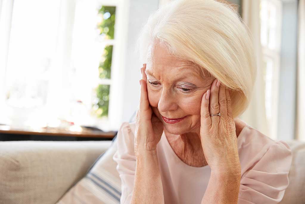 Senior Woman Sitting On Sofa At Home Suffering From Depression