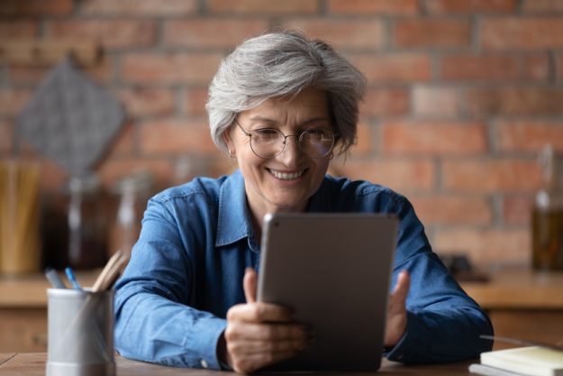 Close up smiling mature woman wearing glasses using computer tablet How To Begin Your Research For Senior Housing In Florida
