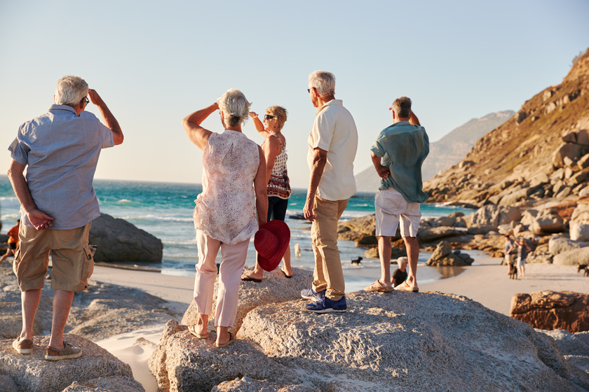 Rear View Of Senior Friends Standing On Rocks On Summer Group Vacation Looking Out To Sea Rear View Of Senior Friends Standing On Rocks On Summer Group Vacation Looking Out To Sea