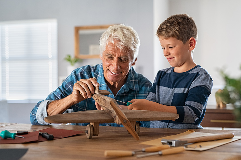 Old grandfather and child assembling wooden plane together