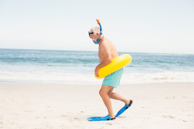 Senior man with swimming ring and flippers at the beach