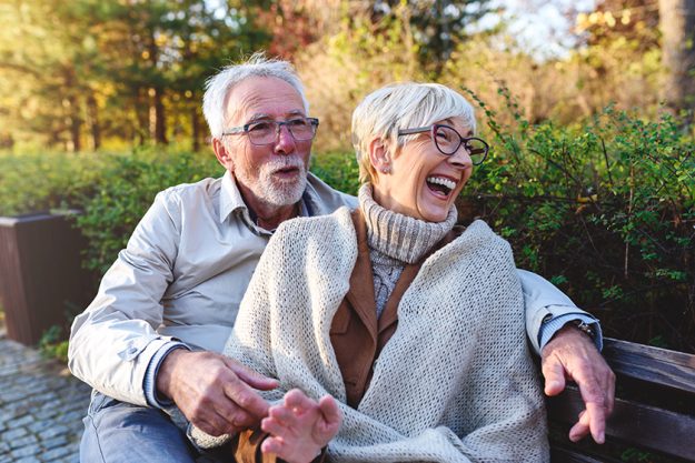 Smiling senior couple sitting on the bench in the park together enjoying retirement Smiling senior couple sitting on the bench in the park together enjoying retirement