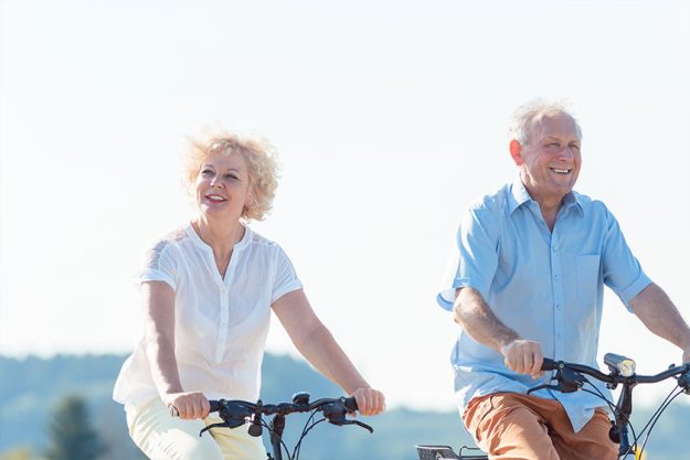 Active elderly couple wearing summer casual clothes while riding bicycles