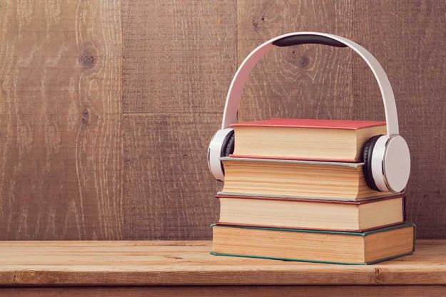 Audio books concept with stack of old book and headphones on wooden table Audio books concept with stack of old book and headphones on wooden table