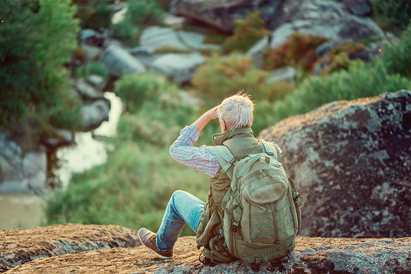 Back view of the old man tourist with a gray hair, sitting on rocks