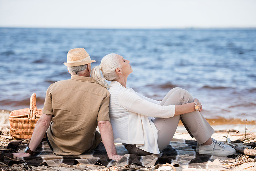 Beautiful senior couple sitting together on plaid at sandy beach Beautiful senior couple sitting together on plaid at sandy beach