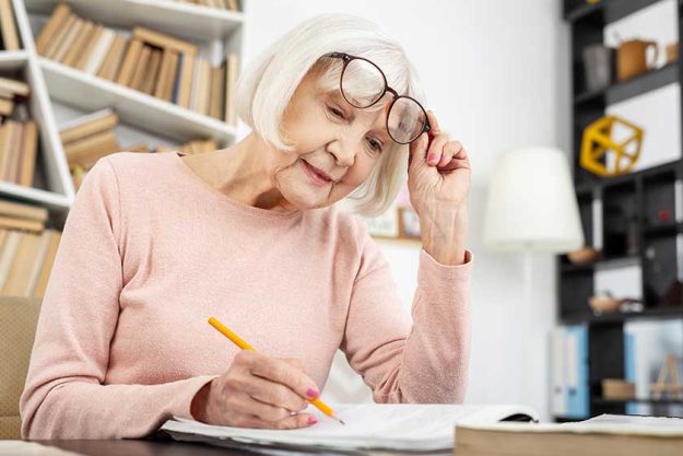 Effective study. Low angle of nice senior woman putting fingers on glasses while learning