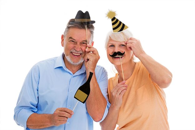 Funny senior couple holding party hats and mustaches on sticks Funny senior couple holding party hats and mustaches on sticks