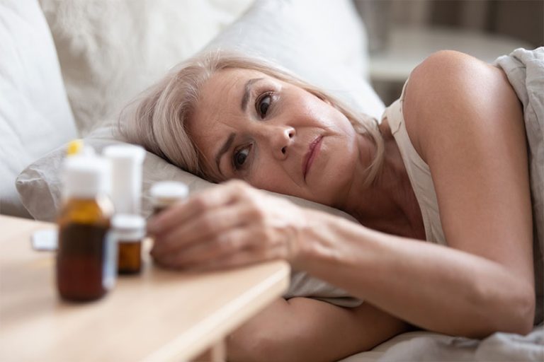 Old woman lying in bed looking at heap of pills