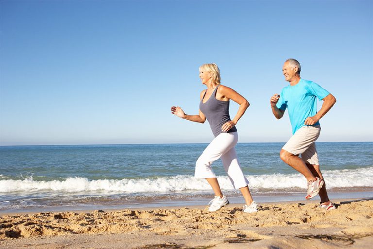 Senior Couple In Fitness Clothing Running Along Beach Senior Couple In Fitness Clothing Running Along Beach