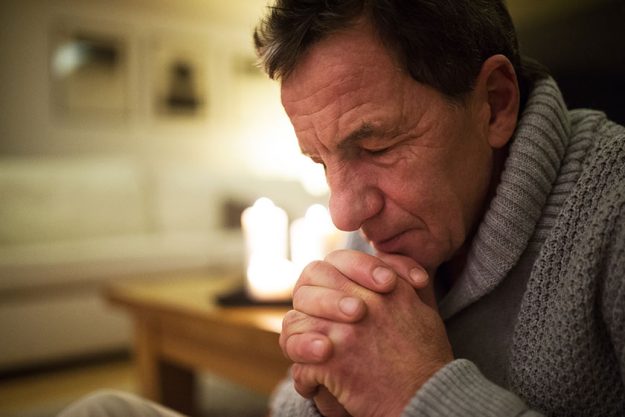 Senior man at home praying, burning candles behind him.