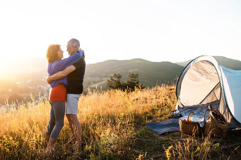Senior tourist couple standing in nature at sunset, hugging.