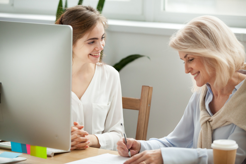 Senior female client signing contract with smiling manager in of