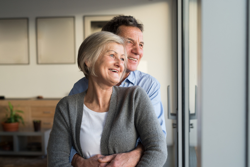 Senior couple in living room standing at the window, hugging Senior couple in living room standing at the window, hugging