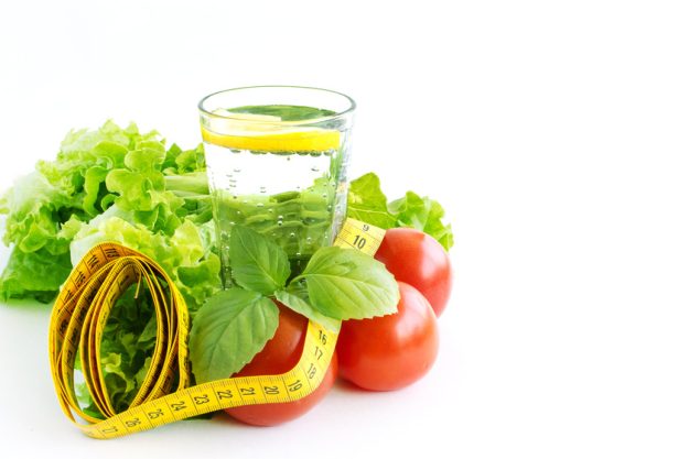 Glass of water with lemon, lettuce and tape measure. Proper nutr Glass of water with lemon, lettuce and tape measure. Proper nutr