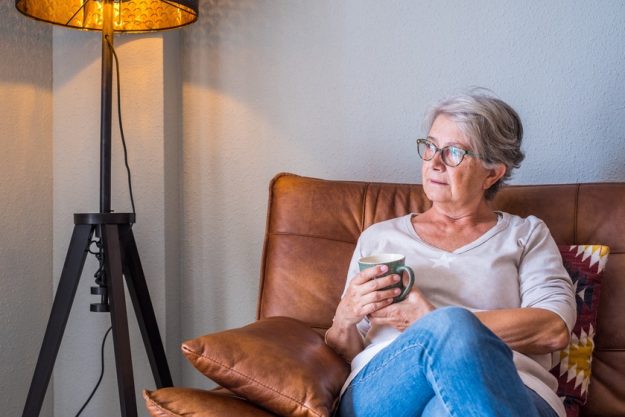 Senior woman sitting on sofa and holding coffee mug while lookin Senior woman sitting on sofa and holding coffee mug while lookin